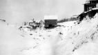 Snow covered riverbed with buildings overhanging undercut banks