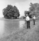 Two Men Fishing Along A River