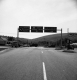 Three Road Signs Over Paved Roadway