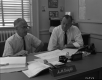 A.M. Kight and Hal Howard Sitting at a Desk